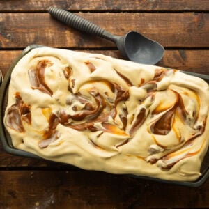 a container of dulce de leche ice cream swirled with dulce de leche with an ice cream soup on the side