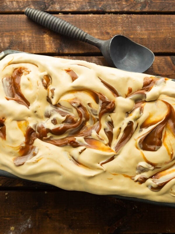 a container of dulce de leche ice cream swirled with dulce de leche with an ice cream soup on the side