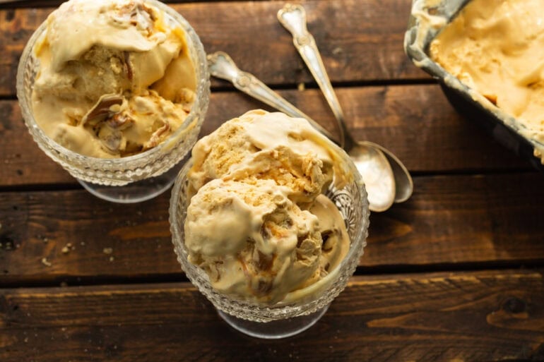 two small glass ice cream dishes full of creamy dulce de leche ice cream with two spoons sitting on the side