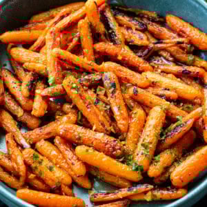 a photo of a large blue serving bowl full of honey garlic roasted baby carrots sprinkled with chopped herbs