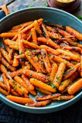 a photo of a large blue serving bowl full of honey garlic roasted baby carrots sprinkled with chopped herbs