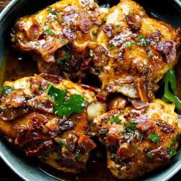 a photo of a skillet with 4 golden chicken thighs topped with bacon and chopped parsley