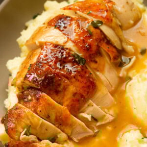 a photo of a golden roasted chicken breast that has been sliced sitting on tope of mashed potatoes covered in gravy.