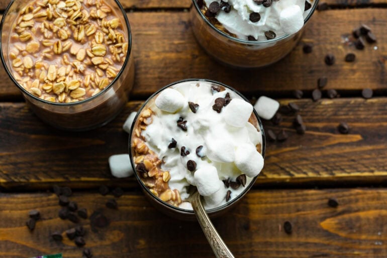 several small jars filled with chocolate overnight oats and topped with whipped cream, mini chocolate chips and mini marshmallows
