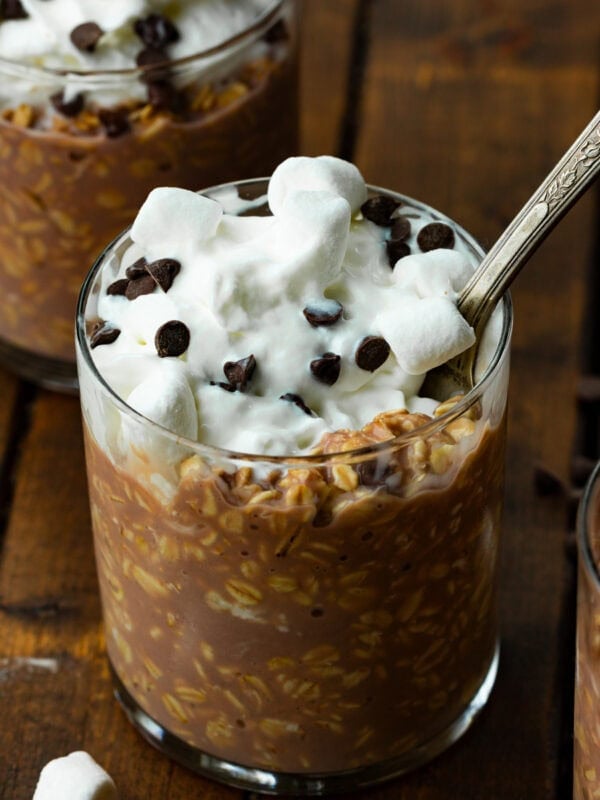 a small glass cup full of hot cocoa overnight oats topped with whipped cream and sprinkled with mini chocolate chips