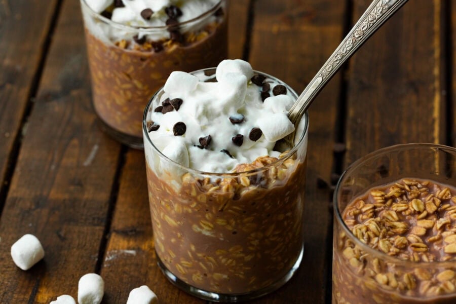 a small glass cup full of hot cocoa overnight oats topped with whipped cream and sprinkled with mini chocolate chips
