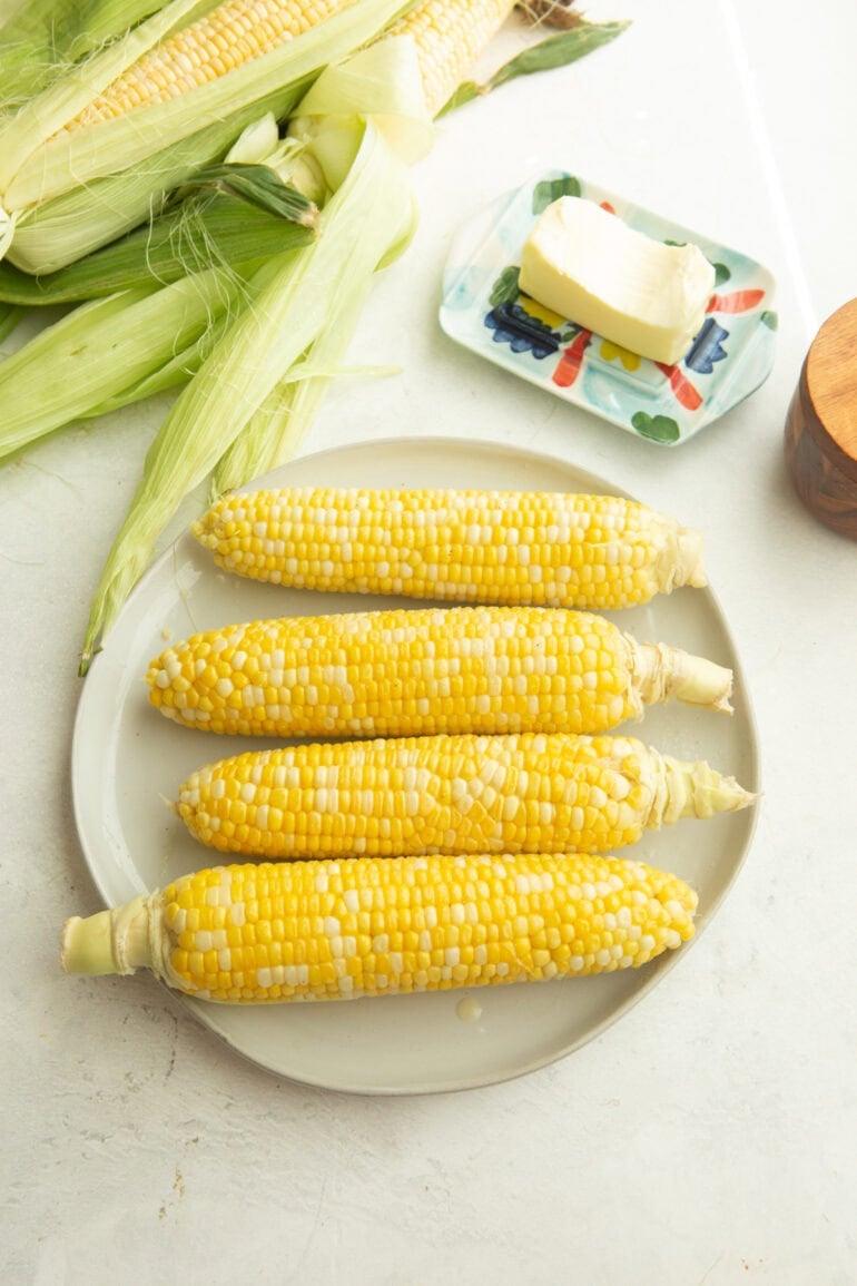 four ears of corn on a plate with a stick of butter next to the plate