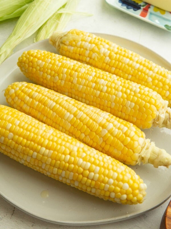 four ears of corn sitting on a dinner plate with bright yellow kernels
