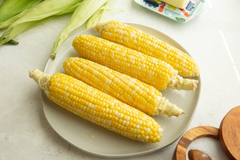 four ears of corn sitting on a dinner plate with bright yellow kernels