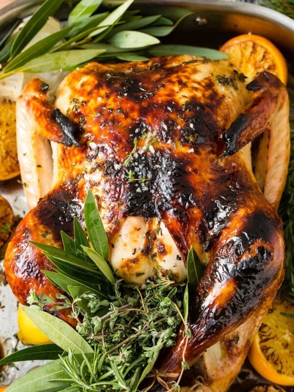 A photo of a whole roasted turkey on a platter surrounded by roasted lemon halves and bunches of fresh herbs.