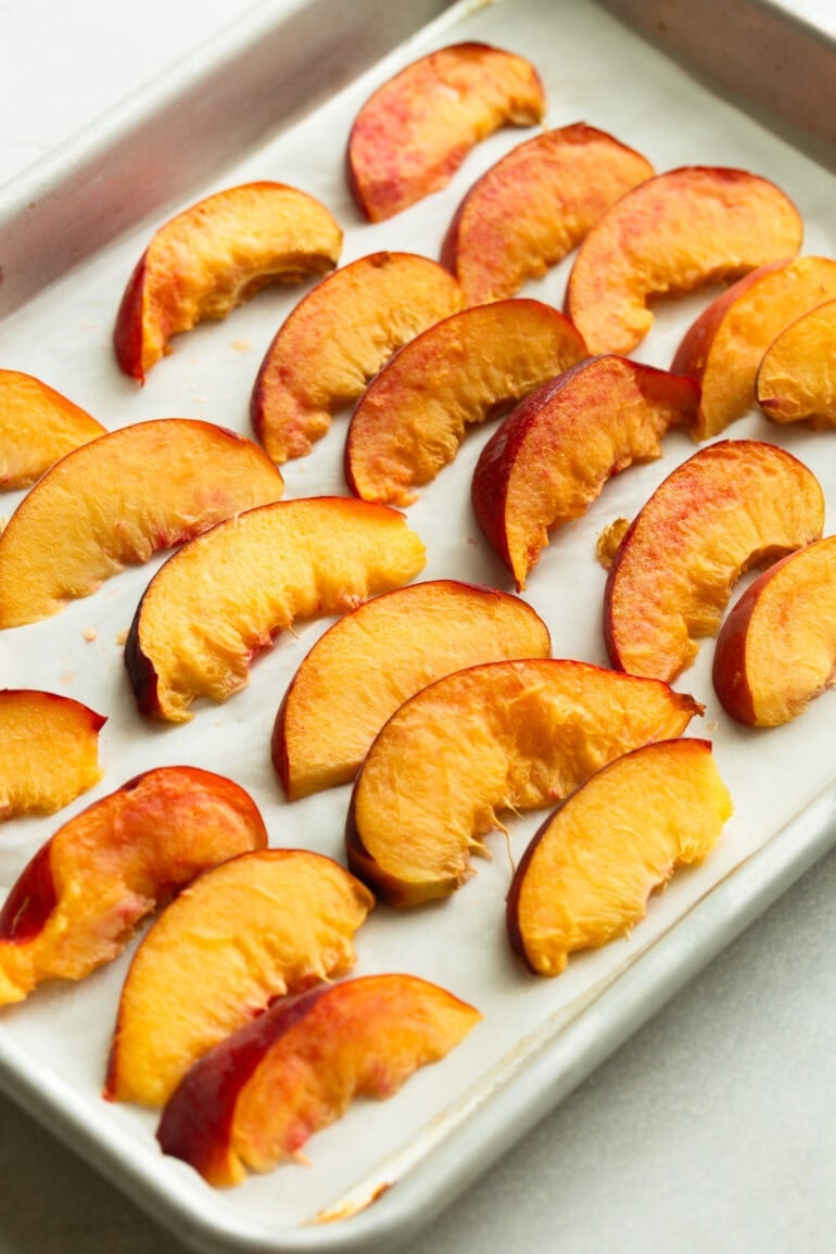 Primer plano de rodajas de durazno espaciadas uniformemente en una bandeja para hornear, preparadas para la congelación de flash.