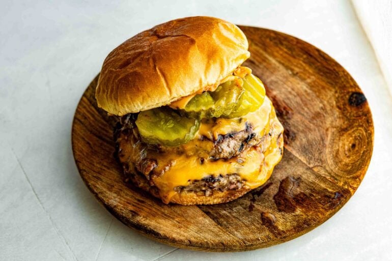a juicy, double patty cheeseburger with metly cheese and dill pickle rounds on a toasted brioche bun