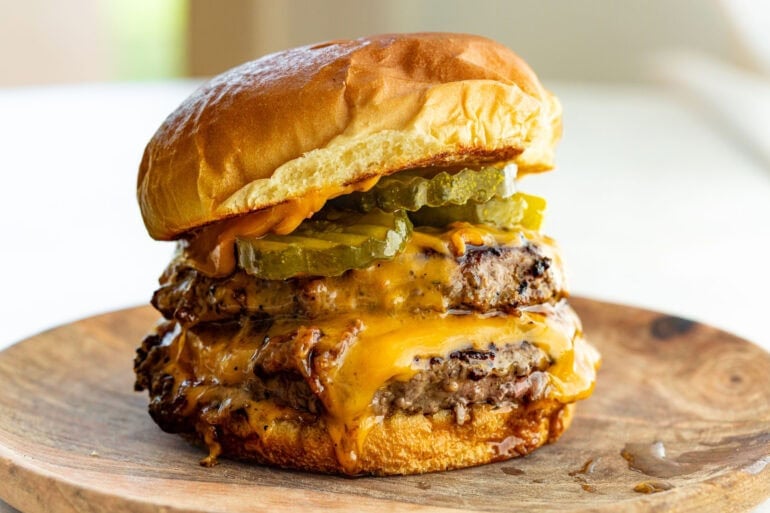 a perfectly grilled burger with two patties, melted cheese pickles and a toasted bun