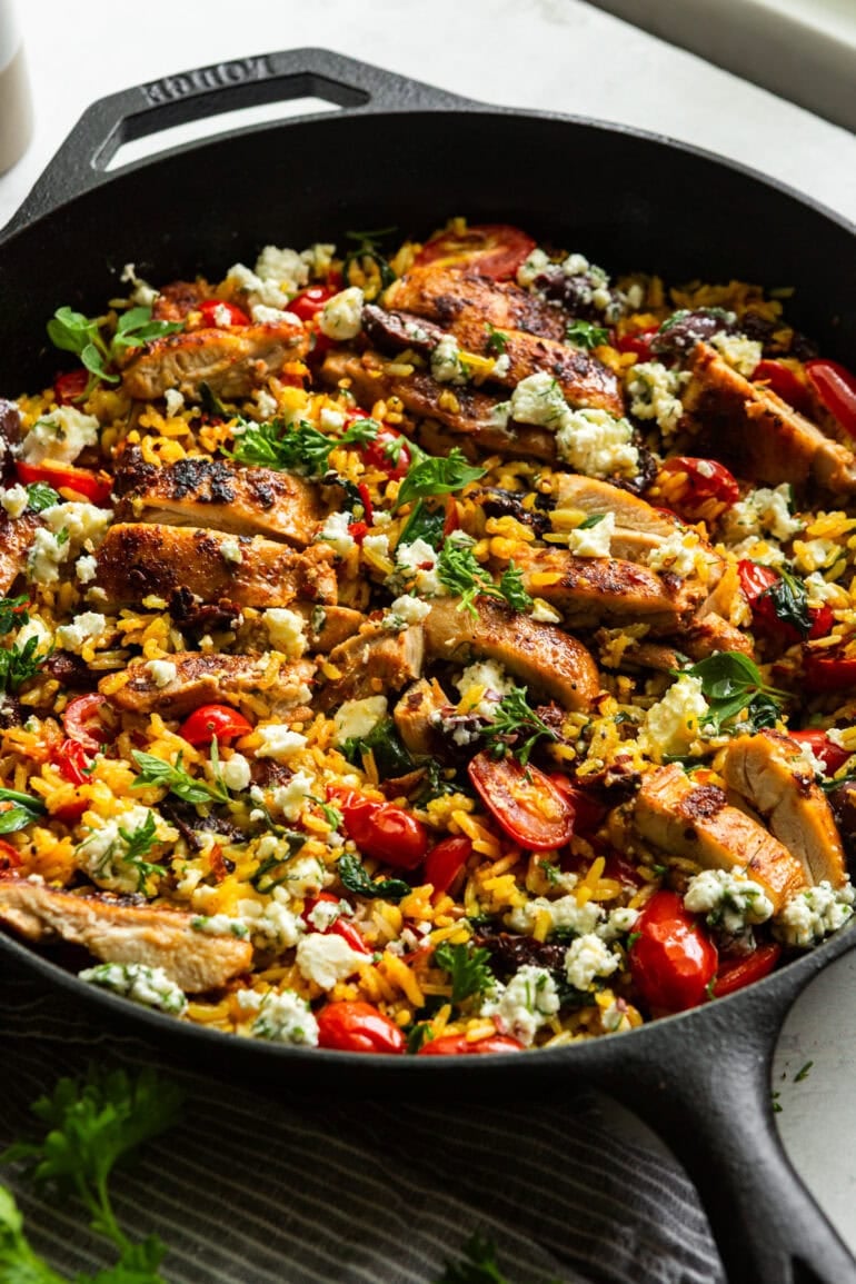A cast iron pan with cooked Greek rice, tomatoes, herbs, feta, and grilled chicken