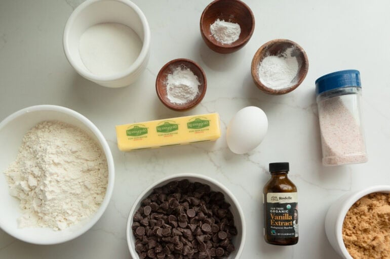 the ingredients for thick chocolate chip cookies including butter, sugar, flour, baking powder and soda, vanilla, an egg, and chocolate chips
