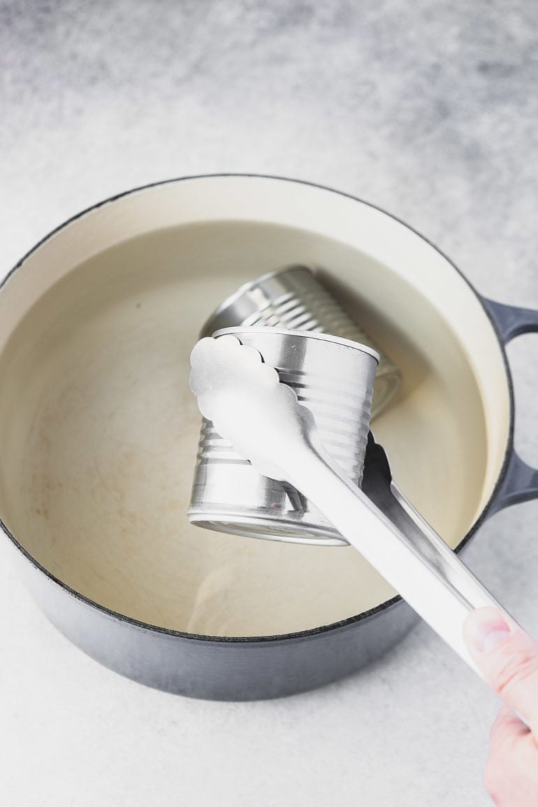 a photo of a pair of metal tongs removing a closed can out of a pot of water