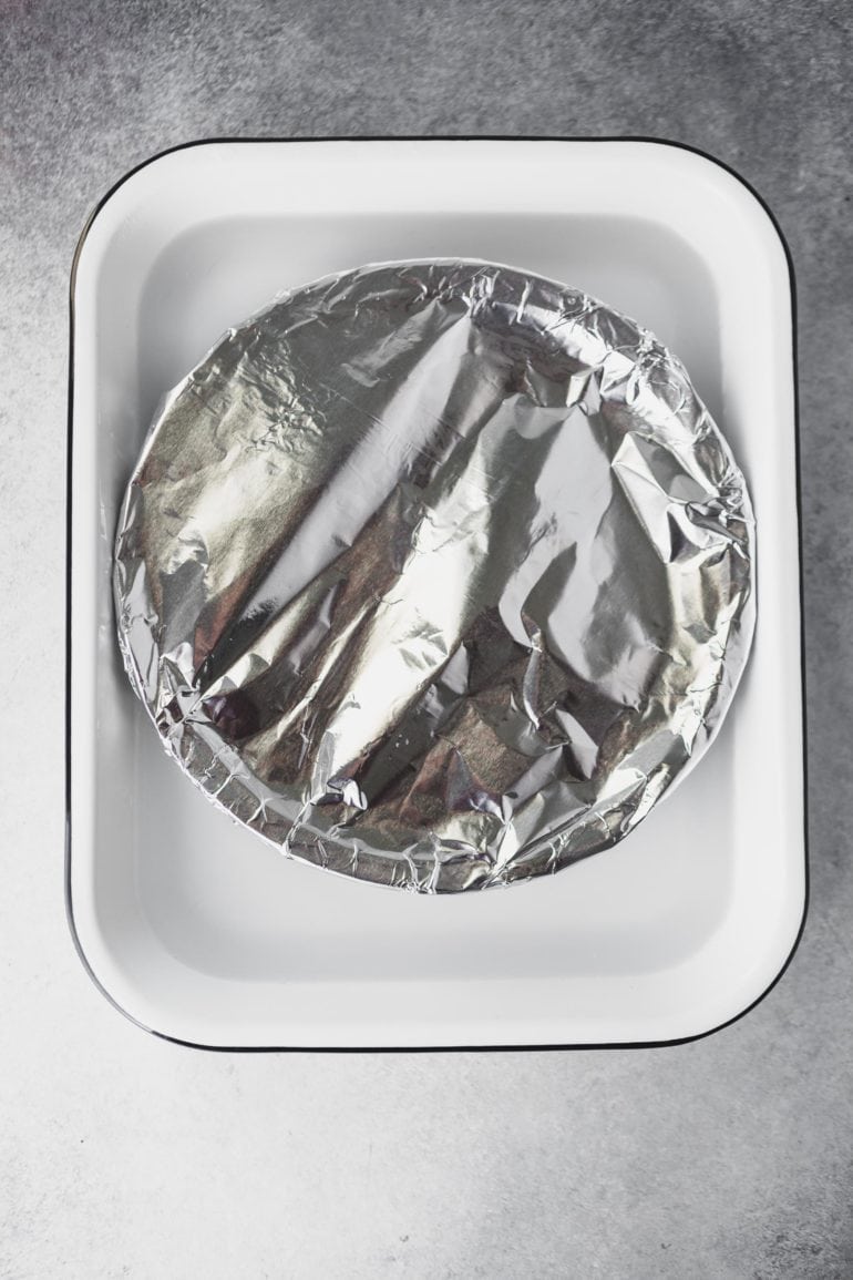 a photo of a pie plate covered with foil sitting in a casserole dish half full of water