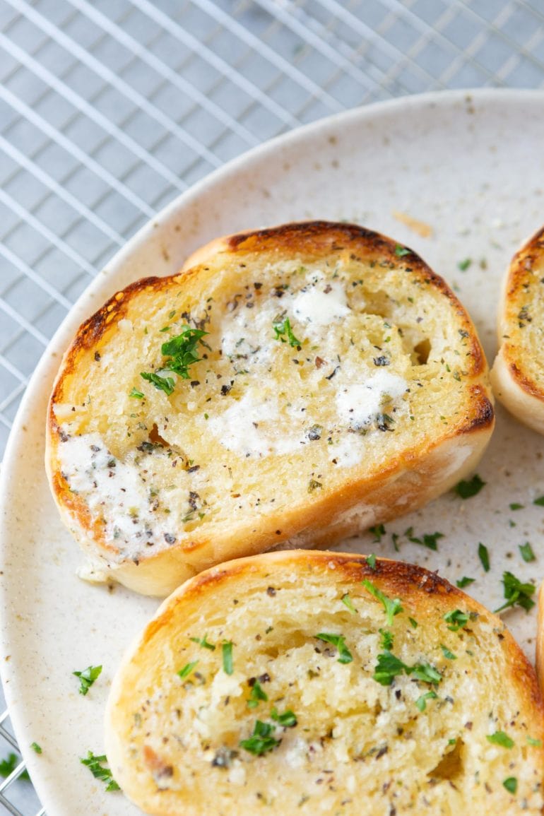 a photo of several slices of buttery toasted garlic bread sprinkled with chopped parsely sitting on a white plate