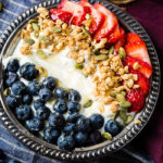 Instant pot homemade yogurt in a vintage bowl with a drizzle of honey and granola with pepitas and fresh blueberries and sliced strawberries for a healthy breakfast recipe