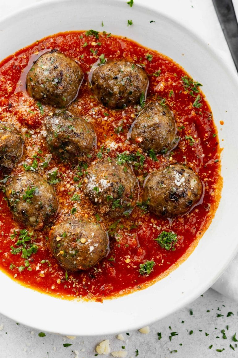 A bowl of meatballs in a tomato based sauce. The dish is sprinkled with chopped parsley.