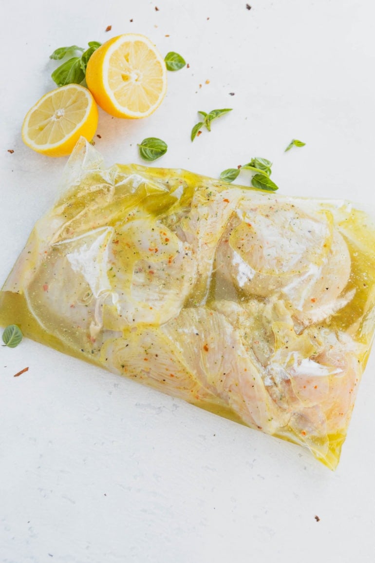 Chicken breasts in marinating in a zip lock bag. Lemon slices are in the background.