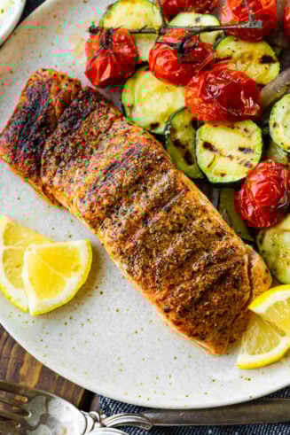 a photo of a perfectly grilled salmon fillet with lemon slices on the side and grilled zucchini and cherry tomatoes