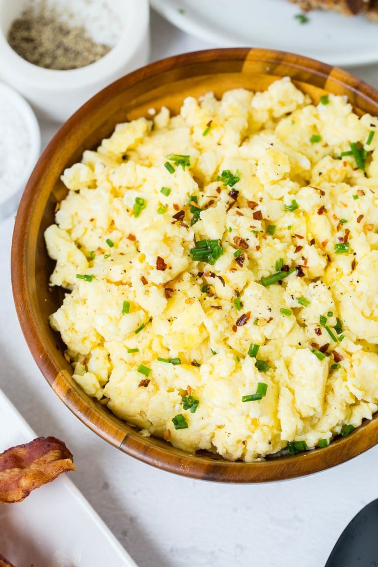 A bowl of fluffy scrambled eggs sprinkled with sliced green onion.