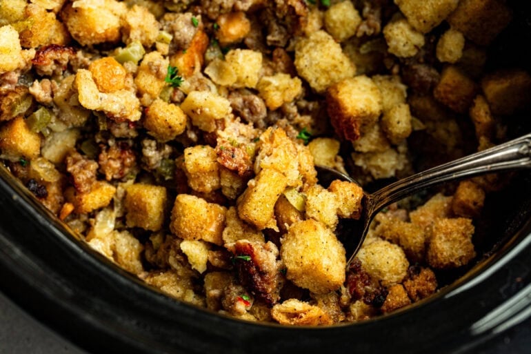 A slow cooker with chunks of bread dressed with sausage, herbs, and veggies for thanksgiving