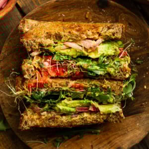 a photo of an avocado sandwich with toasted multigrain bread, bean sprouts, red onions, avocado, arugula, etc.