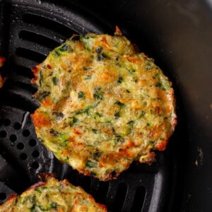 a photo of several golden fried zucchini fritters sitting next to a small cup of creamy dipping sauce