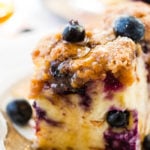 Blueberries on a piece of french toast bake or french toast casserole with maple syrup and a sprinkle of powdered sugar for a breakfast or brunch recipe with a vintage fork and white lace plate. Blueberry french toast bake 3 ways