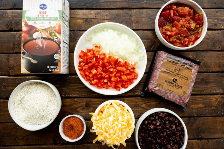 all the ingredients for ground beef burrito bowls in separate small bowls including black beans, shredded cheddar cheese, beef broth, sour cream, etc
