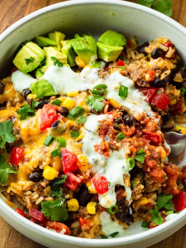 a ground beef burrito bowl topped with sour cream, melted cheese and avocados