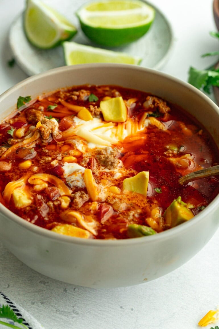 Grey bowl of Instant Pot taco soup on a white countertop, topped with fresh cilantro, sour cream, shredded cheese, and sliced avocado.