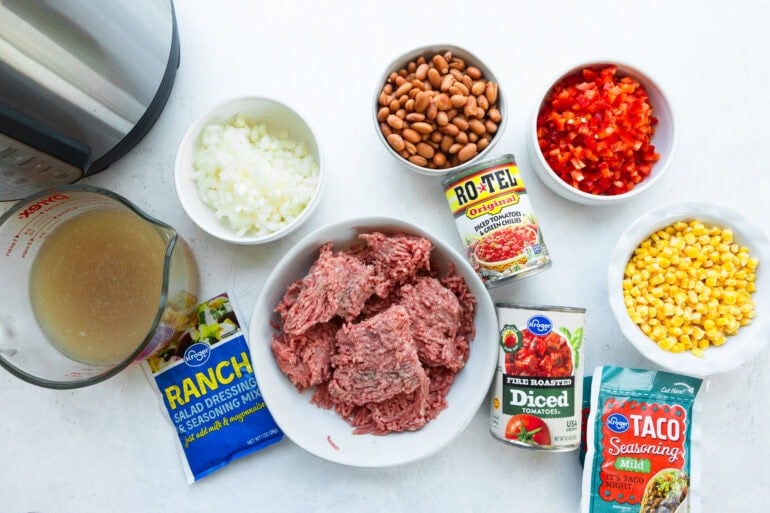 all the ingredients for instant pot taco soup including ground beef, Rotel, pinto beans, cans of diced tomatoes, ranch seasoning powder, diced onions and diced red bell pepper
