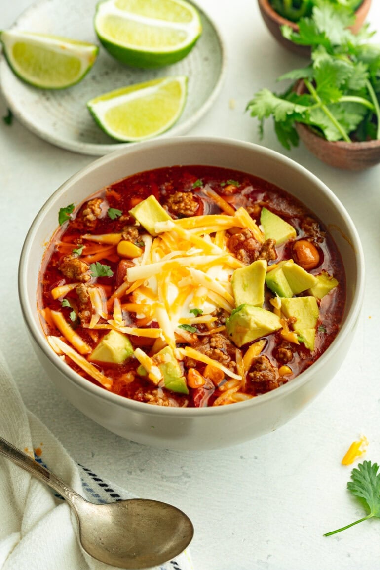 a bowl of taco soup topped with shredded cheddar cheese, sour cream and diced avocado
