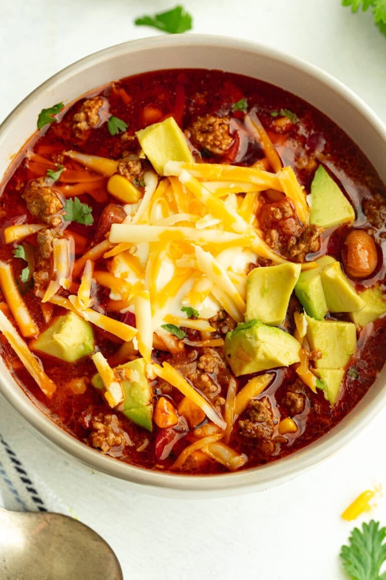 Close-up of taco soup in a grey bowl, garnished with avocado slices, shredded cheese, sour cream, and fresh cilantro.