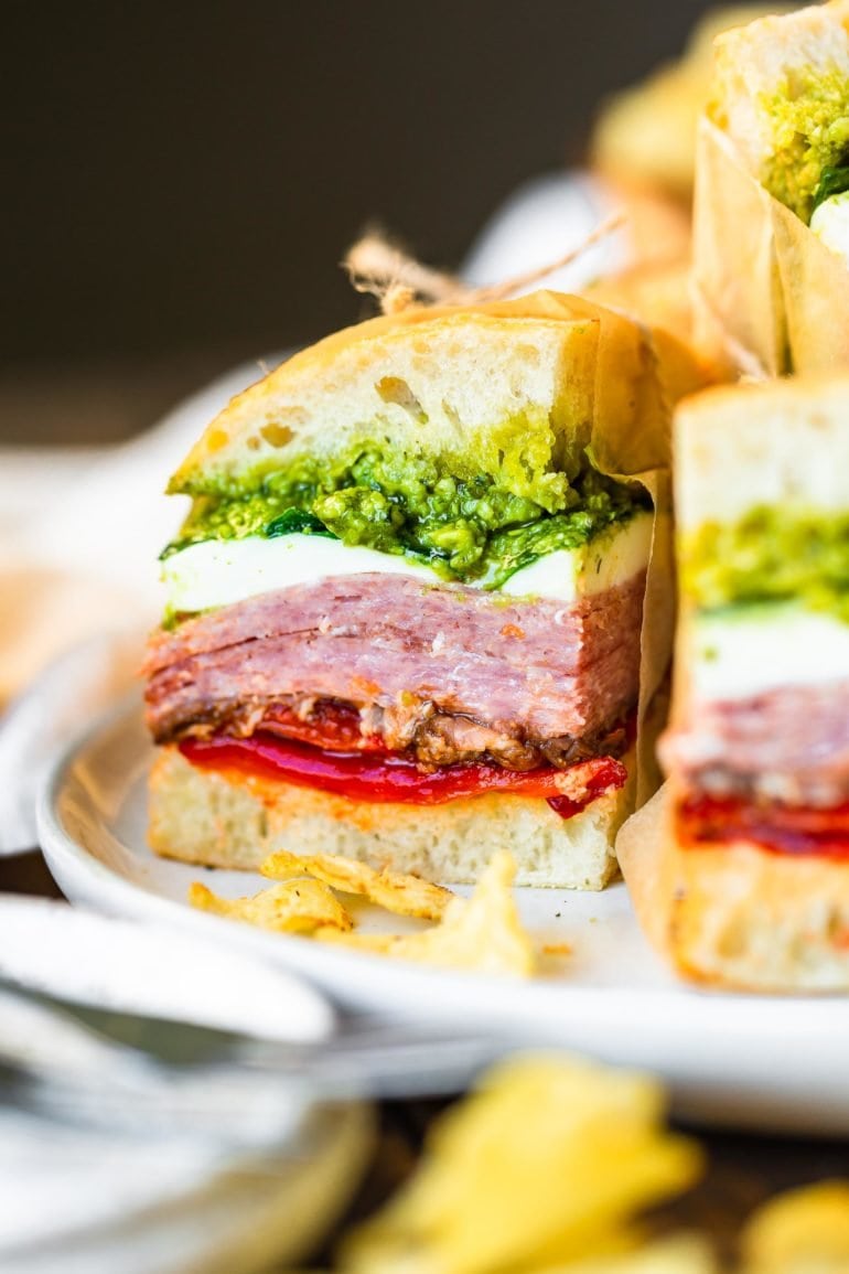 a close up photo of a pressed Italian sandwich stuffed with layers of meat, pesto, fresh mozzarella, roasted red pepper and tomato.
