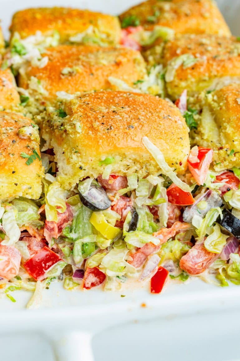 a photo of a baking dish full of baked italian sliders with the front row removed so you can see the inside of the sliders spilling out