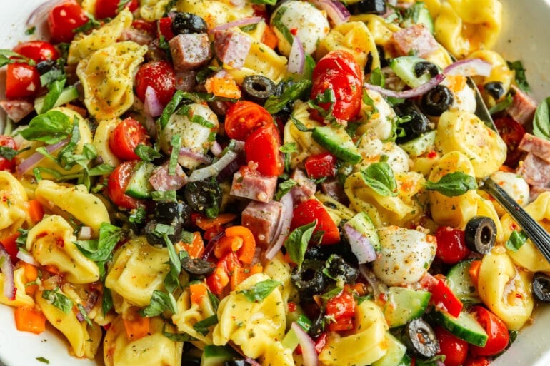 a bowl of tortellini pasta salad with black olives, red onions, tomatoes, cucumber and minced fresh basil