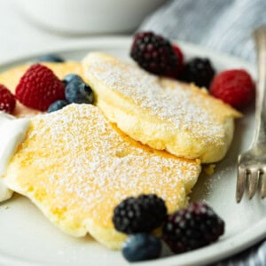 a photo of three fluffy Japanese cloud pancakes topped with powdered sugar and mixed fresh berries