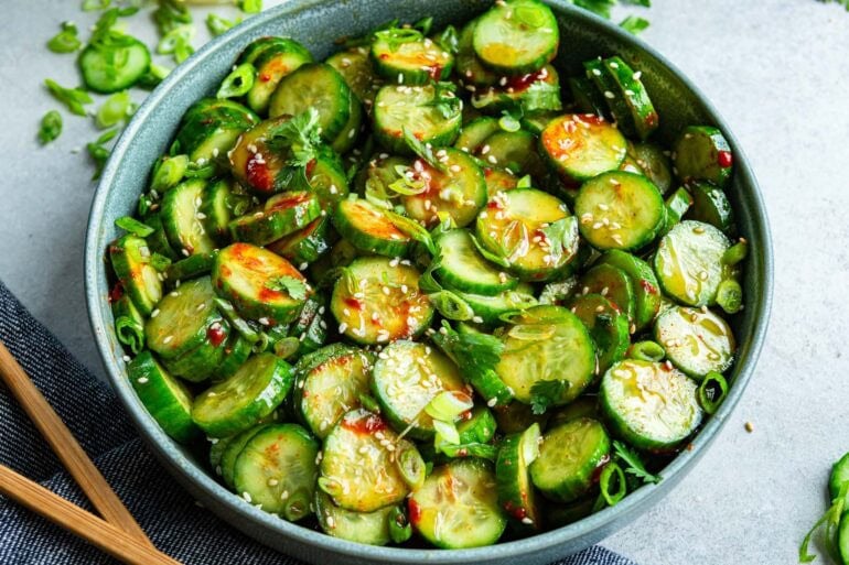 a large bowl of spicy Korean cucumber salad topped with dressing, chopped scallions and sesame seeds