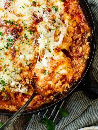 a photo of a serving of skillet lasagna being scooped out of a cast iron skillet