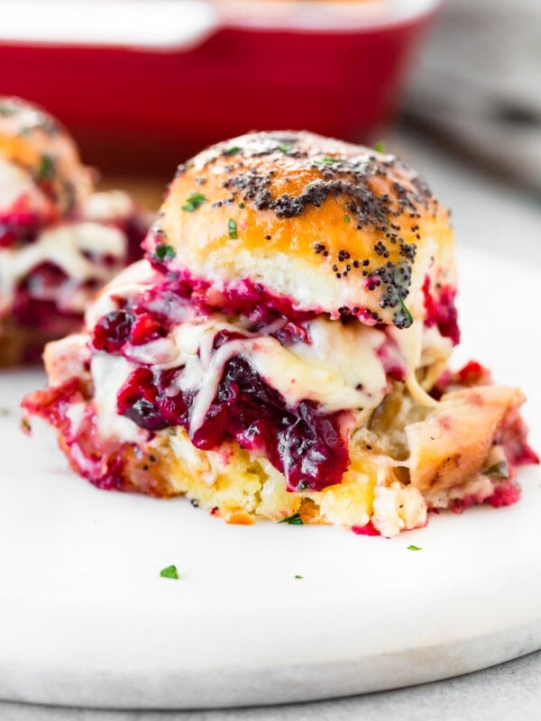 a photo of a turkey cranberry slider covered in a buttery poppyseed dressing with cranberry sauce and melty cheese oozing out the sides