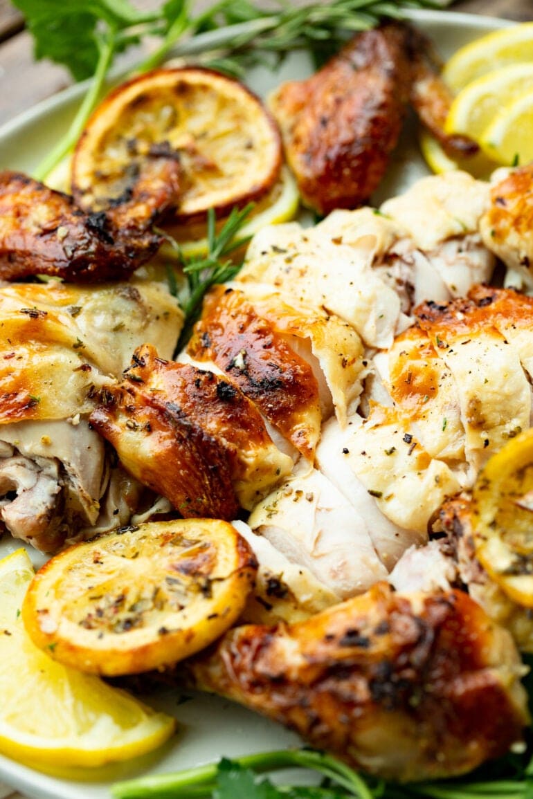 a photo of juicy roasted sliced chicken breasts topped with fresh herbs and surrounded by slices of lemon.
