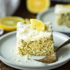 a photo of a piece of lemon poppy seed cake topped with a white cream cheese frosting and small lemon slice