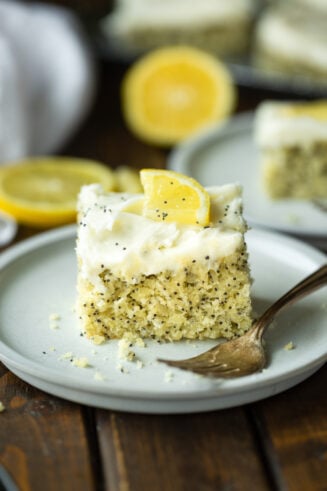 a photo of a piece of lemon poppy seed cake topped with a white cream cheese frosting and small lemon slice