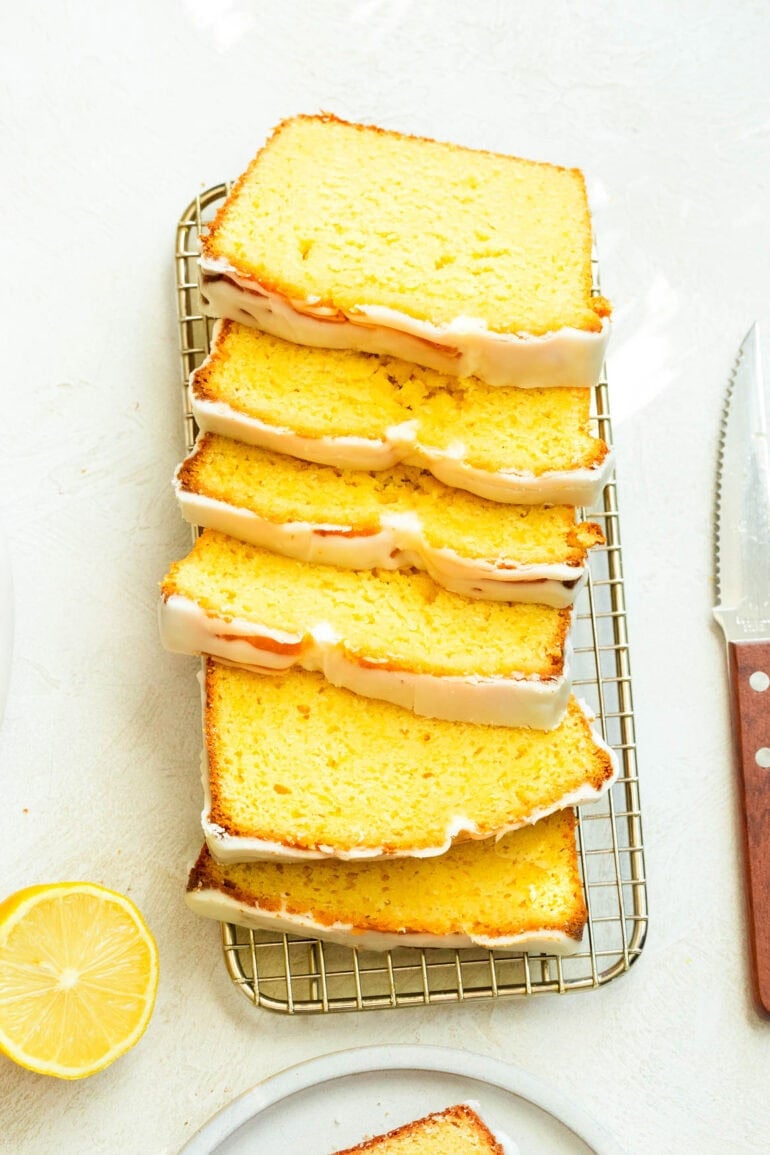 A photo of sliced lemon pound cake stacked on top of each other on a metal cooling rack with a knife next to it