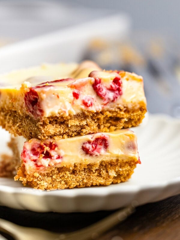 two creamy lemon raspberry bars with graham cracker crust stacked on each other on a small dessert plate