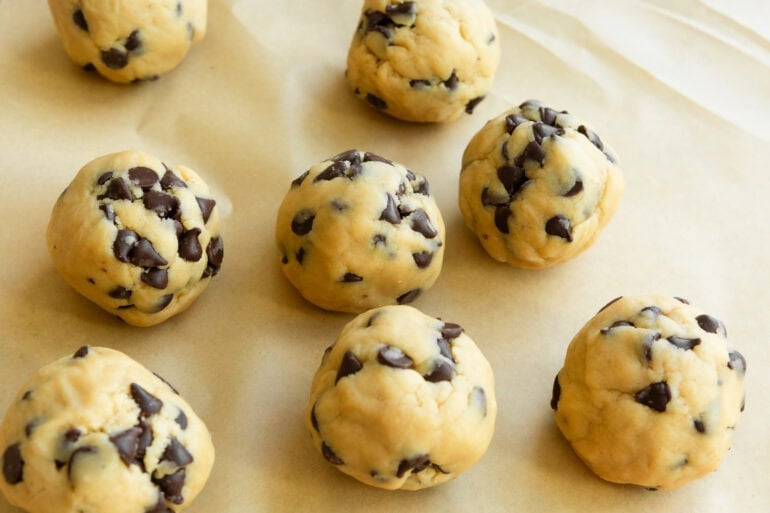 several large balls of chocolate chip cookie dough sitting on a piece of parchment paper